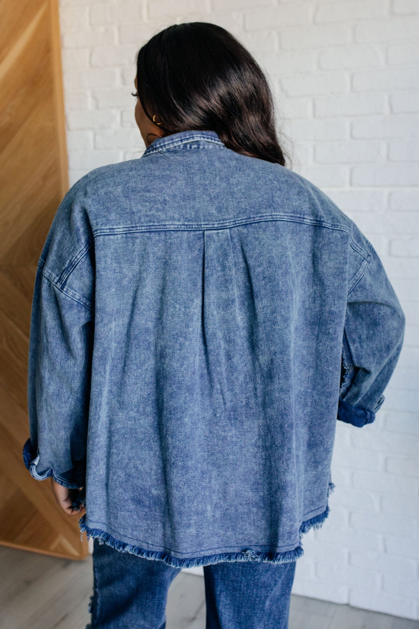 Person wearing a blue denim jacket in front of a white brick wall.