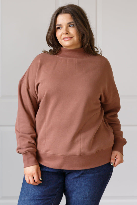 Woman wearing a brown sweatshirt and blue jeans against a white wall