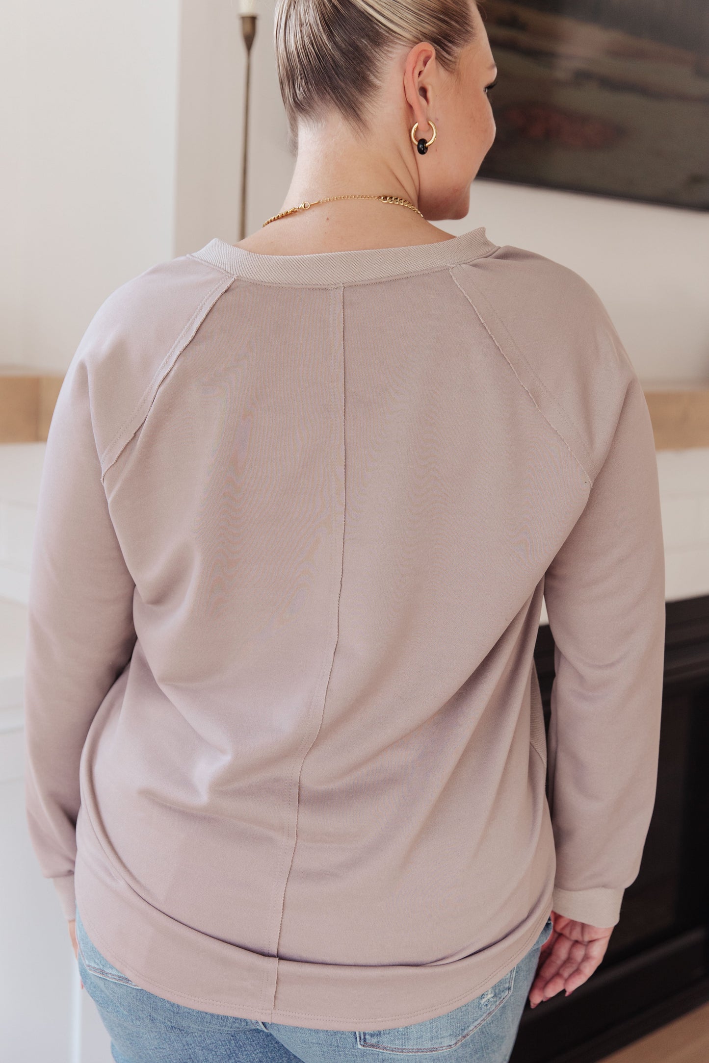 Woman wearing a beige sweater and blue jeans in a bright room.