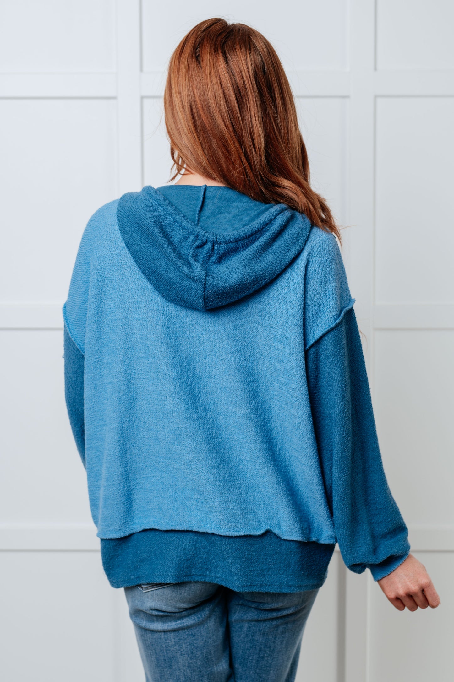 Person wearing a blue hoodie from behind against a white tiled wall
