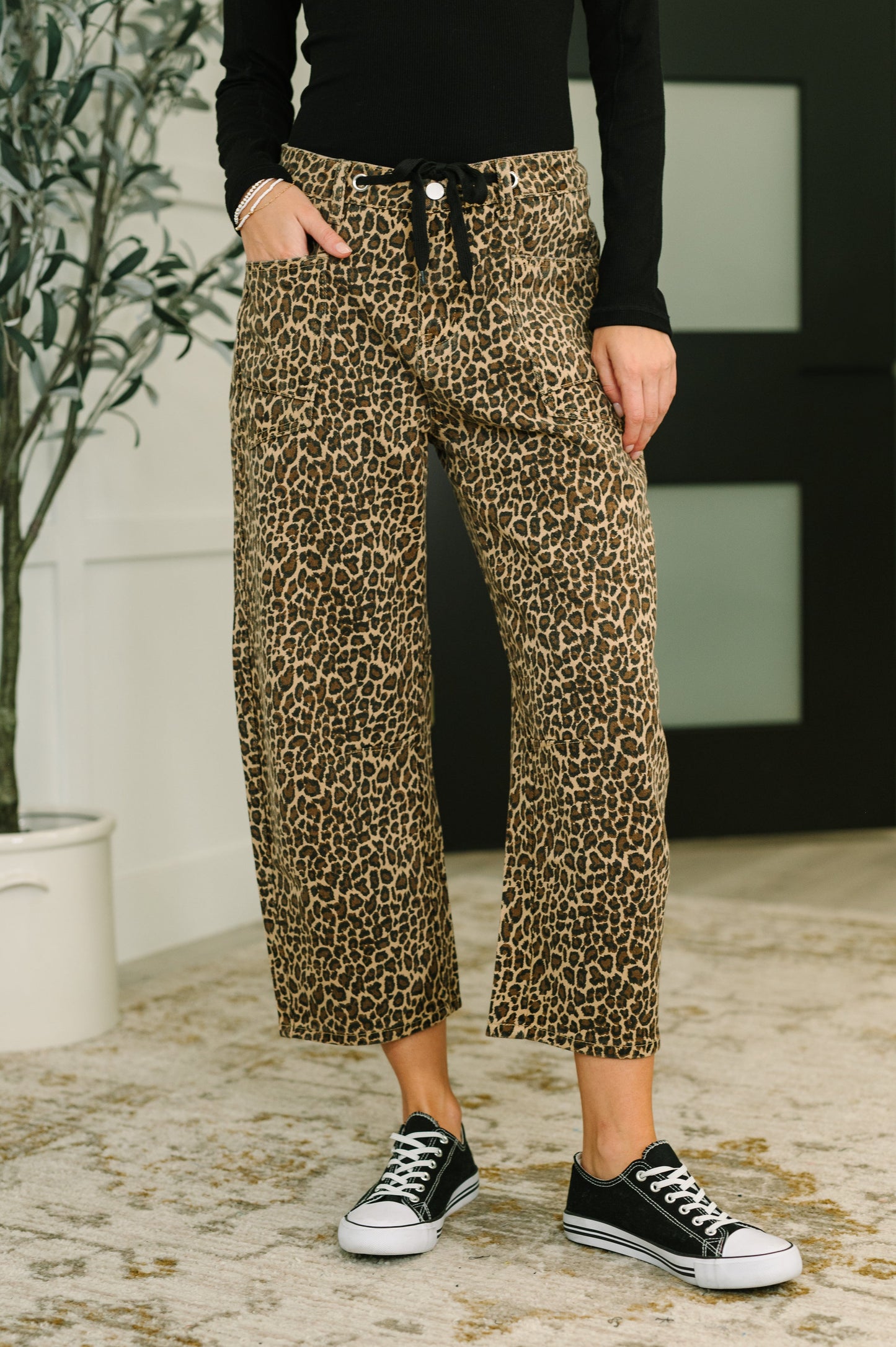 Person wearing leopard print pants and black sneakers indoors.