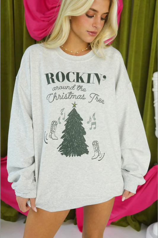 Woman wearing a gray sweatshirt with Christmas-themed design against a green curtain background