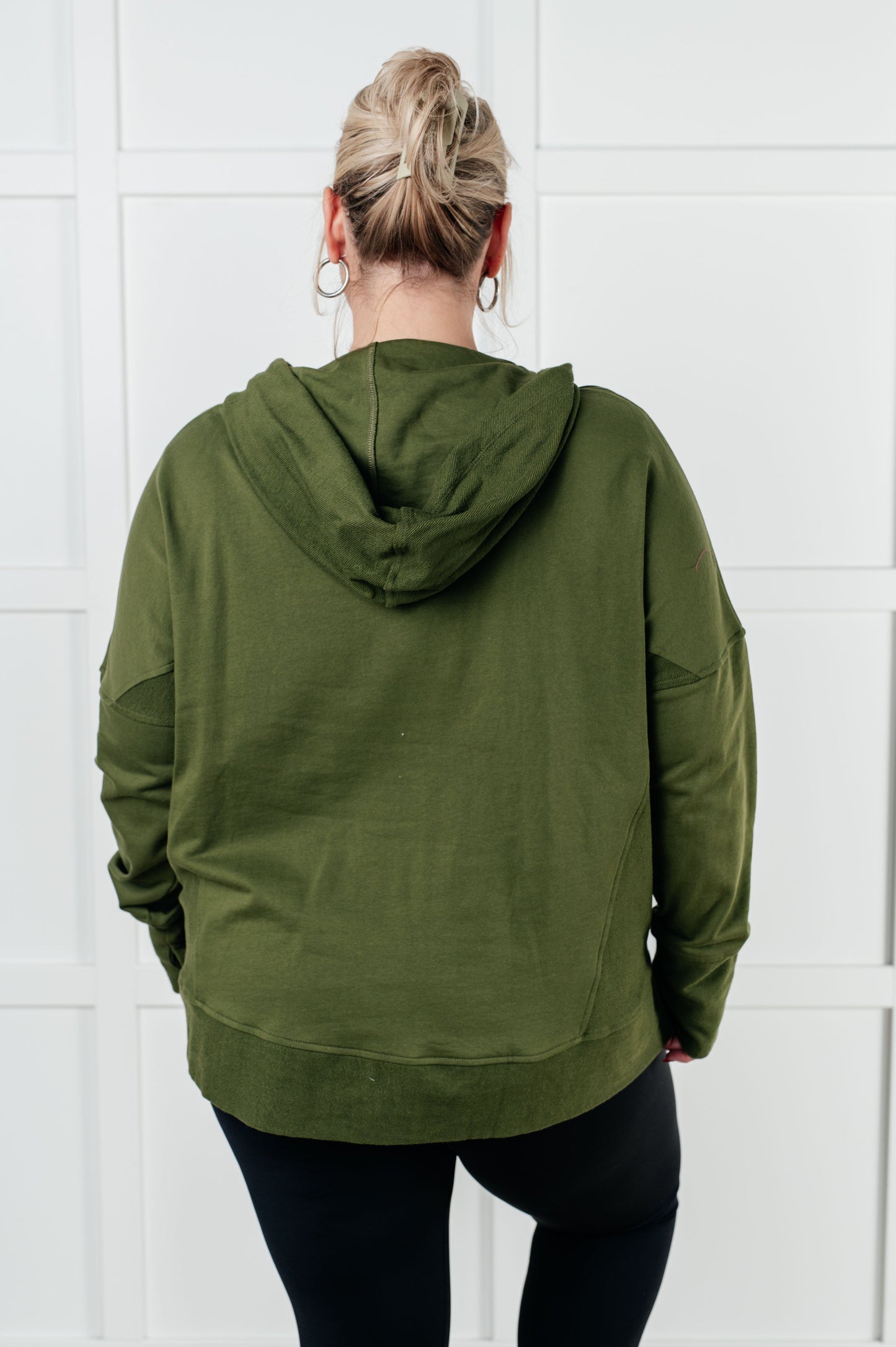 Person wearing an olive green hoodie against a white tiled wall