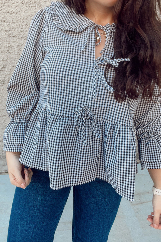 Person wearing a black and white checkered blouse with ruffled details against a neutral background
