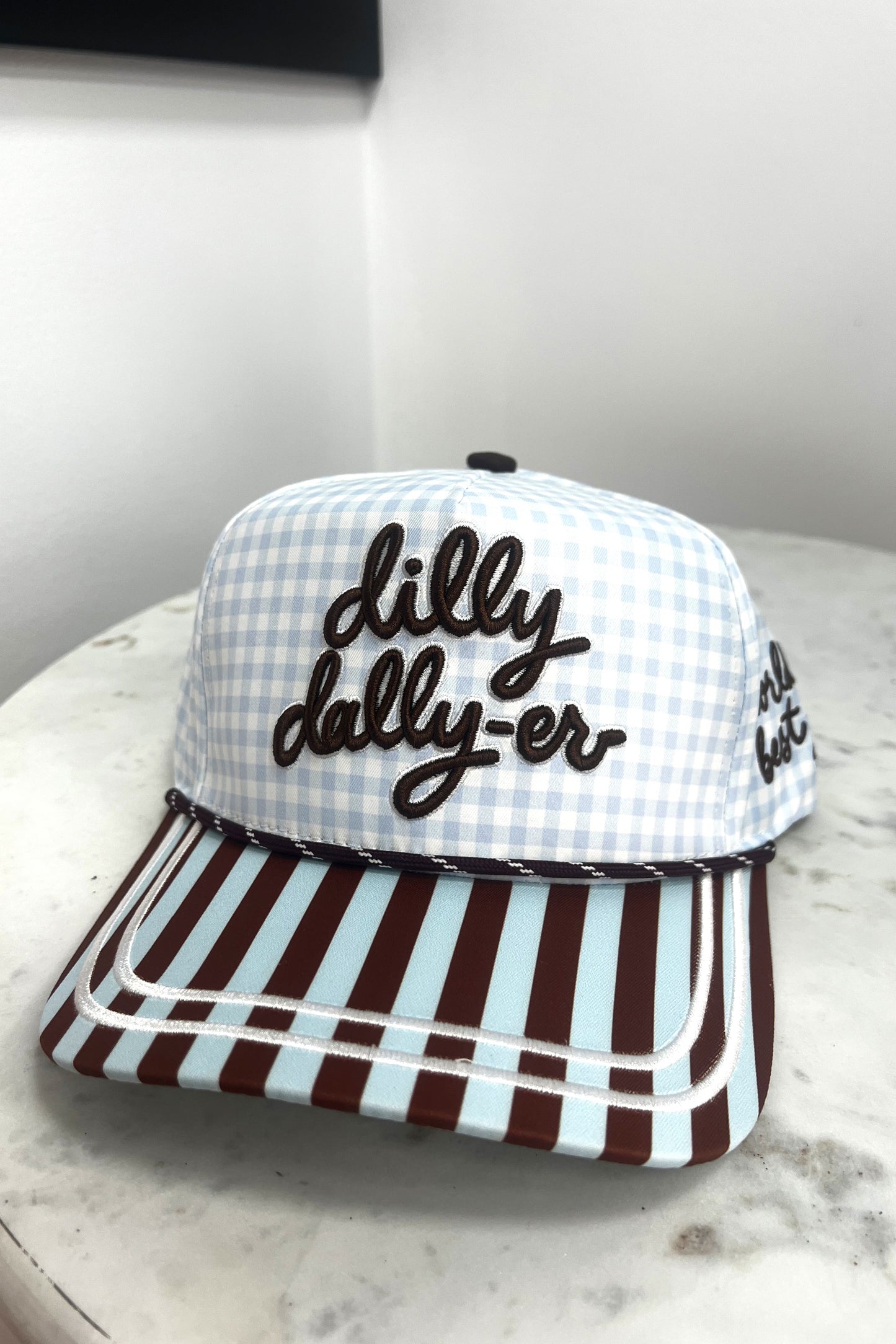 Checkered cap with 'dilly dally-er' text on a marble surface