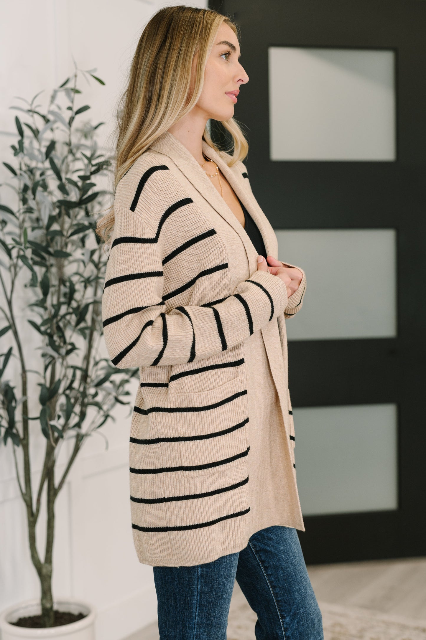 Woman wearing a beige cardigan with black stripes in an indoor setting.