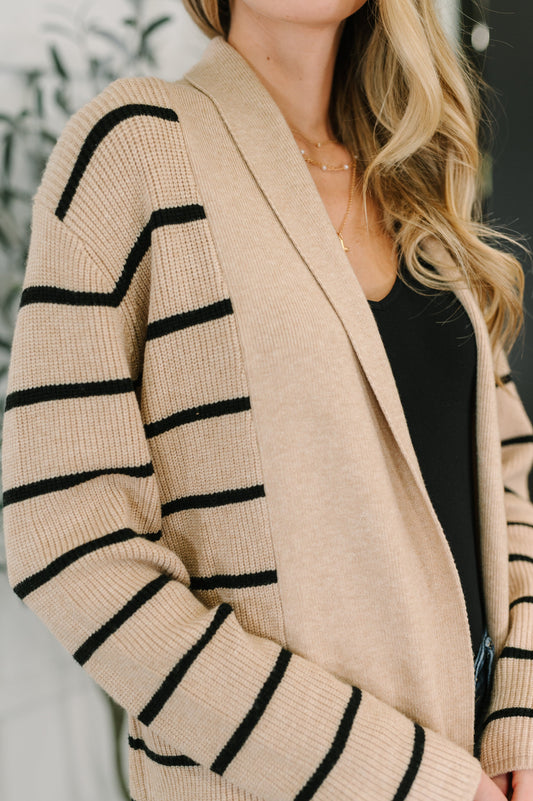 Beige cardigan with black stripes worn by a person, blurred background