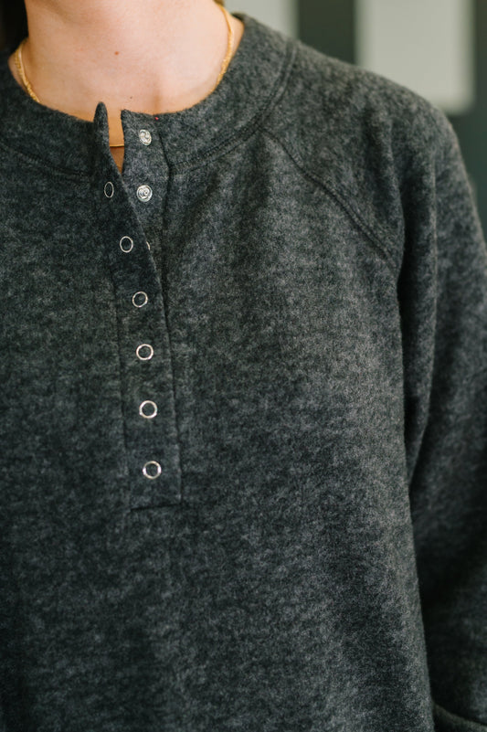 Close-up of a person wearing a dark gray long-sleeve shirt with buttons.
