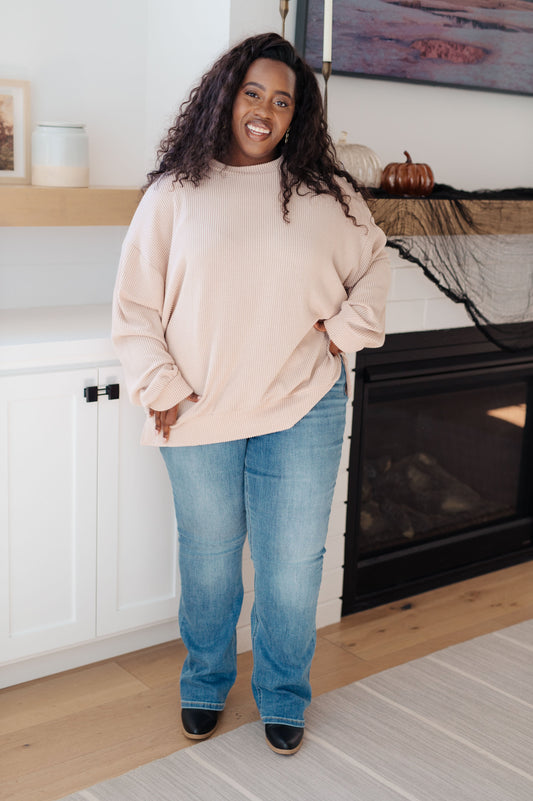 Woman wearing a beige sweater and blue jeans standing in a living room.