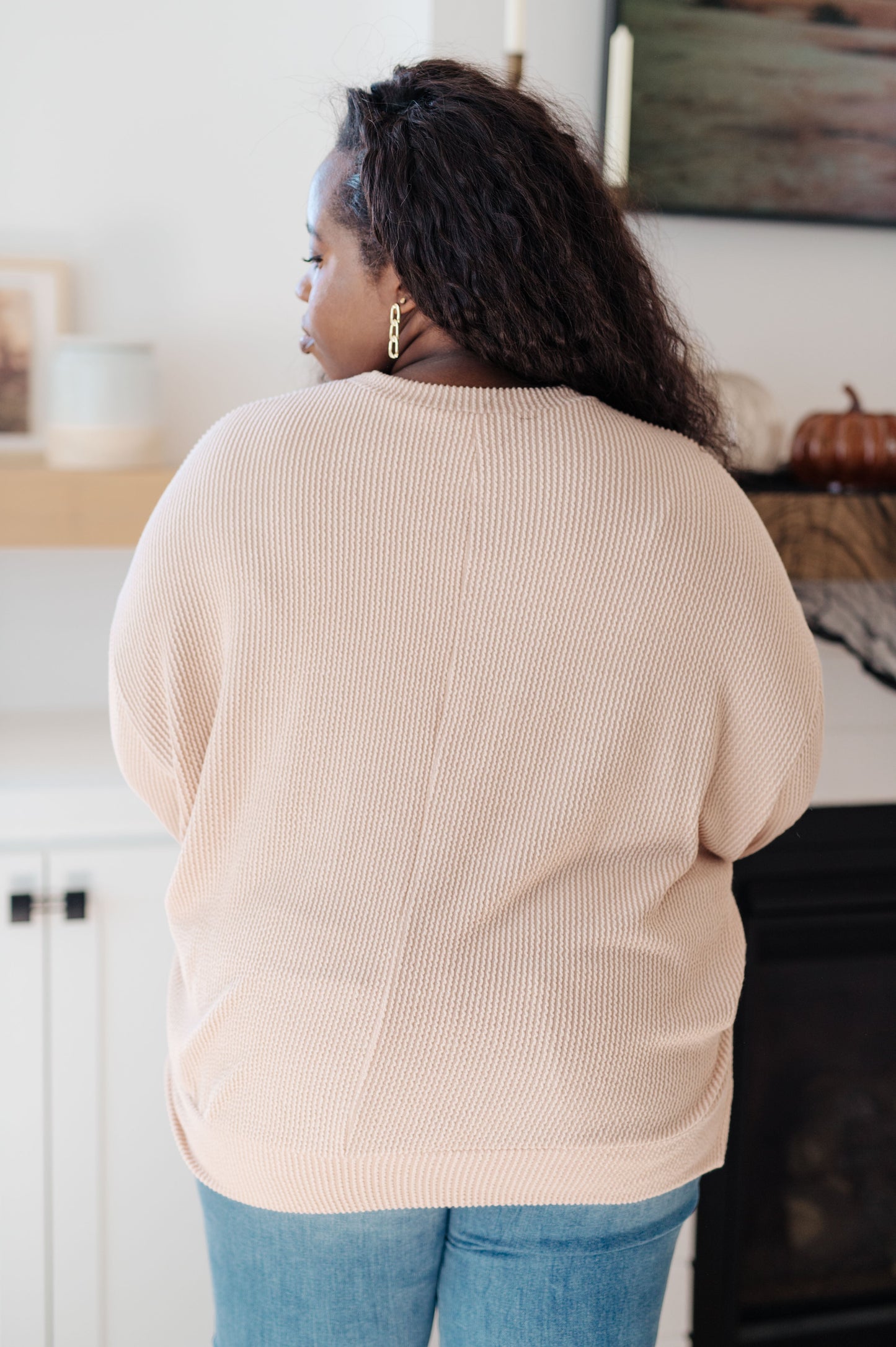 Person wearing a beige sweater and blue jeans in a kitchen setting