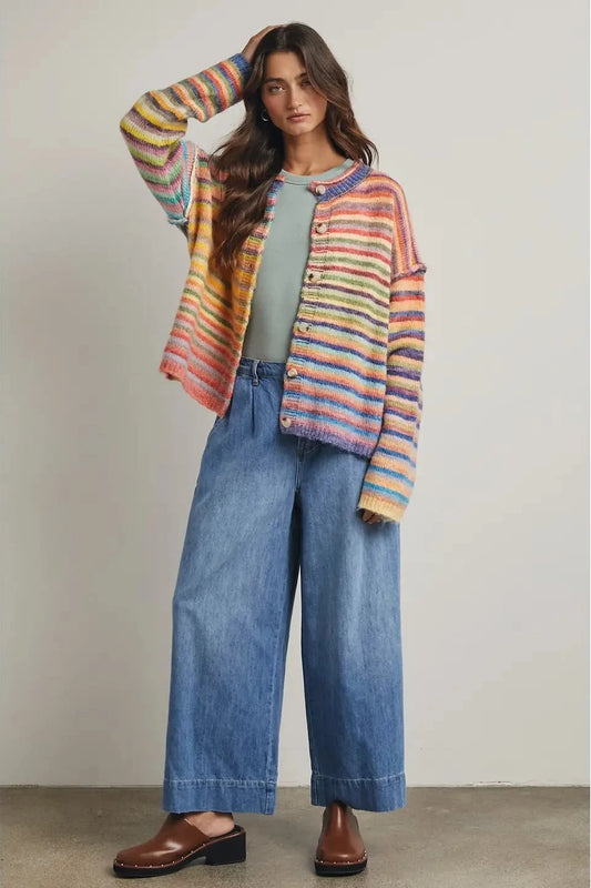 Woman wearing a colorful striped cardigan, green top, and blue jeans against a neutral background