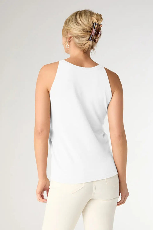 Woman wearing a white sleeveless top and white pants on a plain background