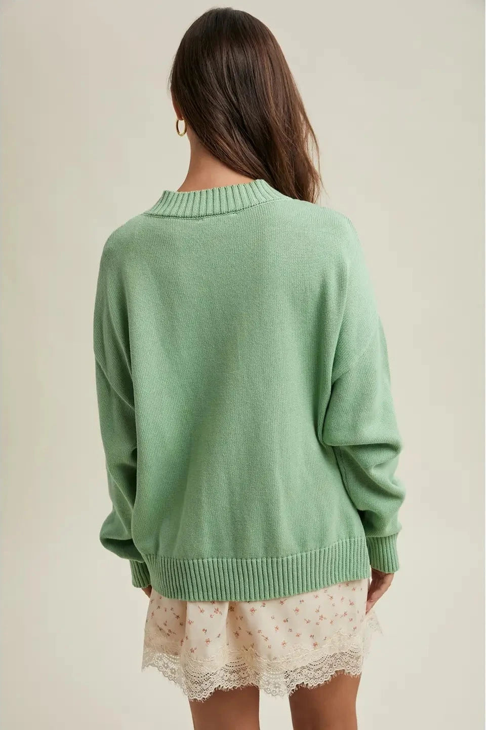 Person wearing a green sweater and lace skirt on a plain background