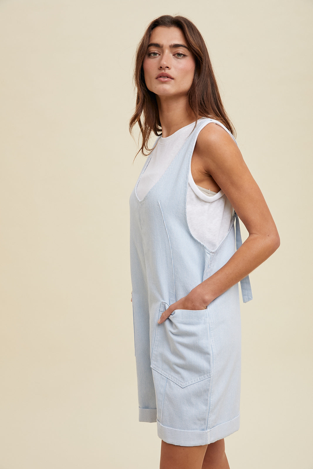 Woman wearing a light blue sleeveless dress with a white pocket on a beige background