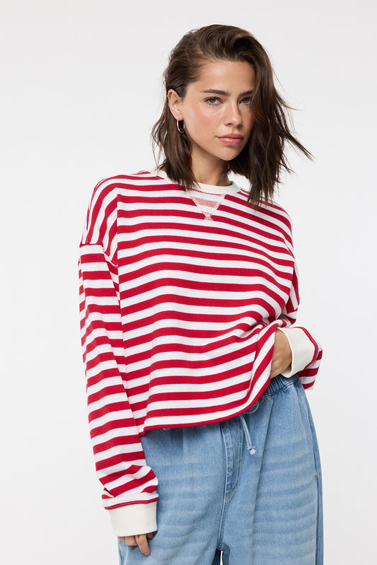 Woman wearing a red and white striped sweater with light blue jeans on a white background
