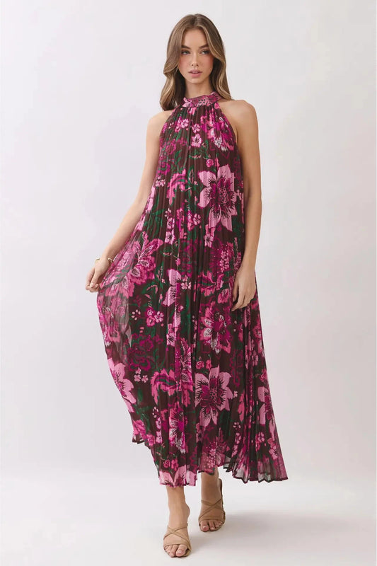A woman modeling a sleeveless halter-neck midi dress with a dark green background and a vibrant pink floral print, paired with beige strappy sandals against a light gray studio background.