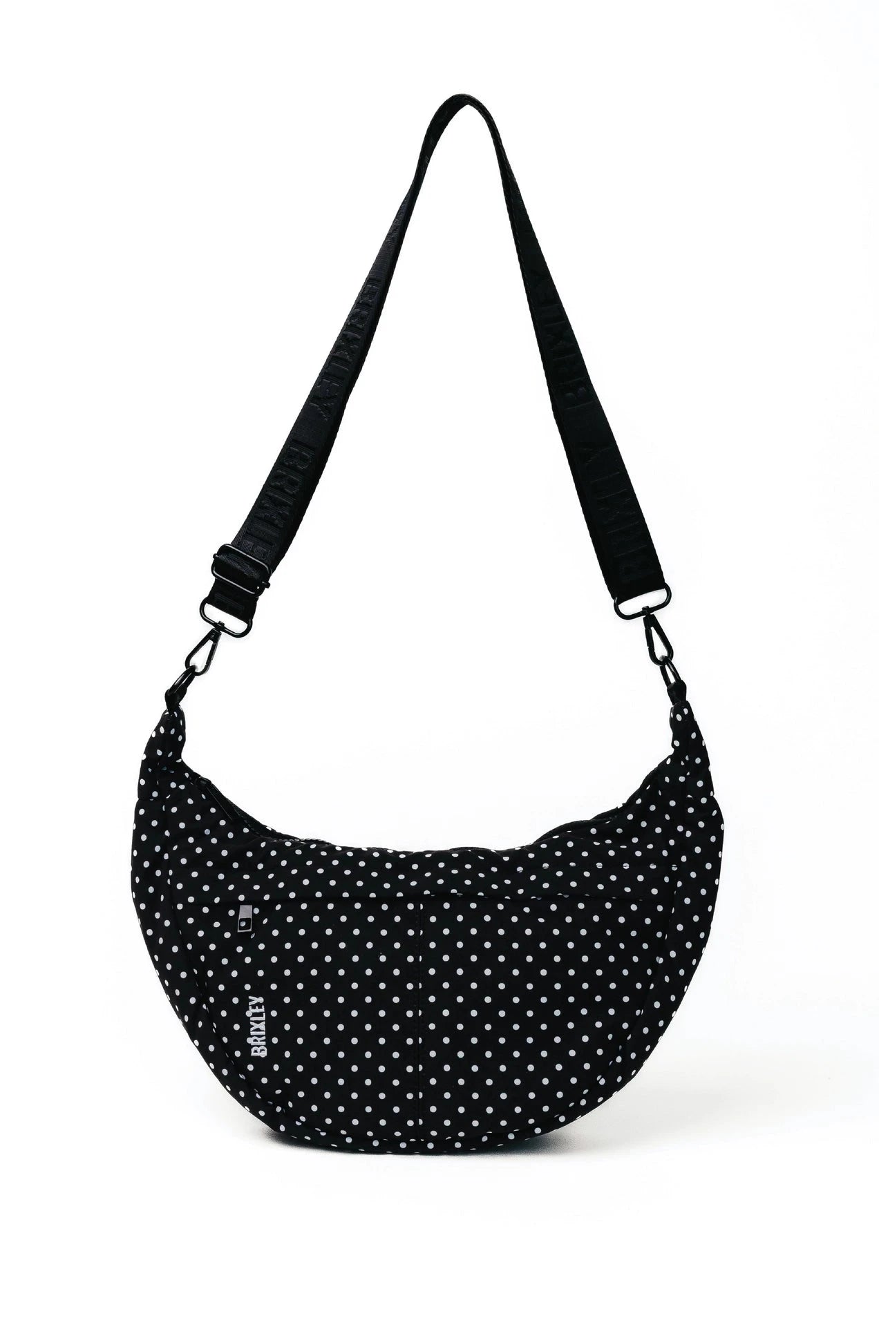 A black crescent-shaped shoulder bag with a white polka dot pattern and an adjustable black strap, shown on a plain white background.