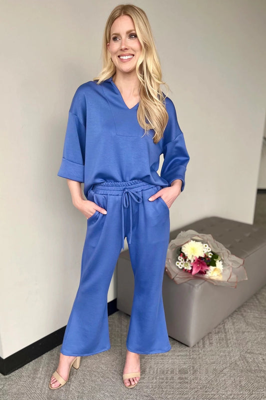 Woman wearing a blue outfit standing next to a gray ottoman with flowers on it.