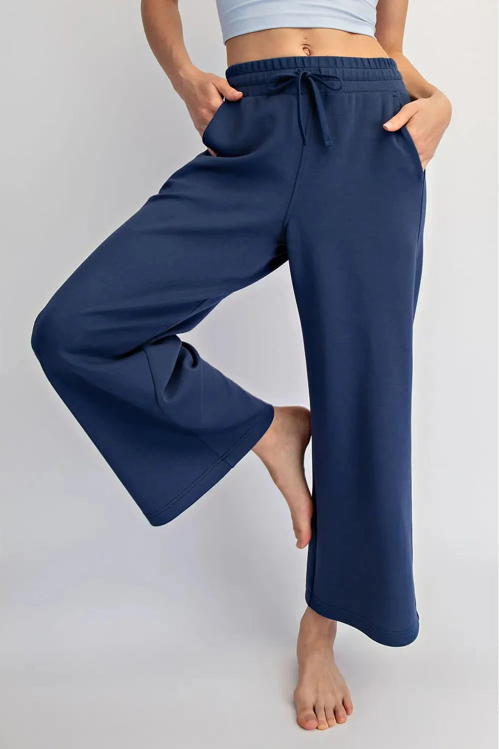 A person wearing navy blue wide-leg drawstring pants, shown from the waist down against a light gray studio background.