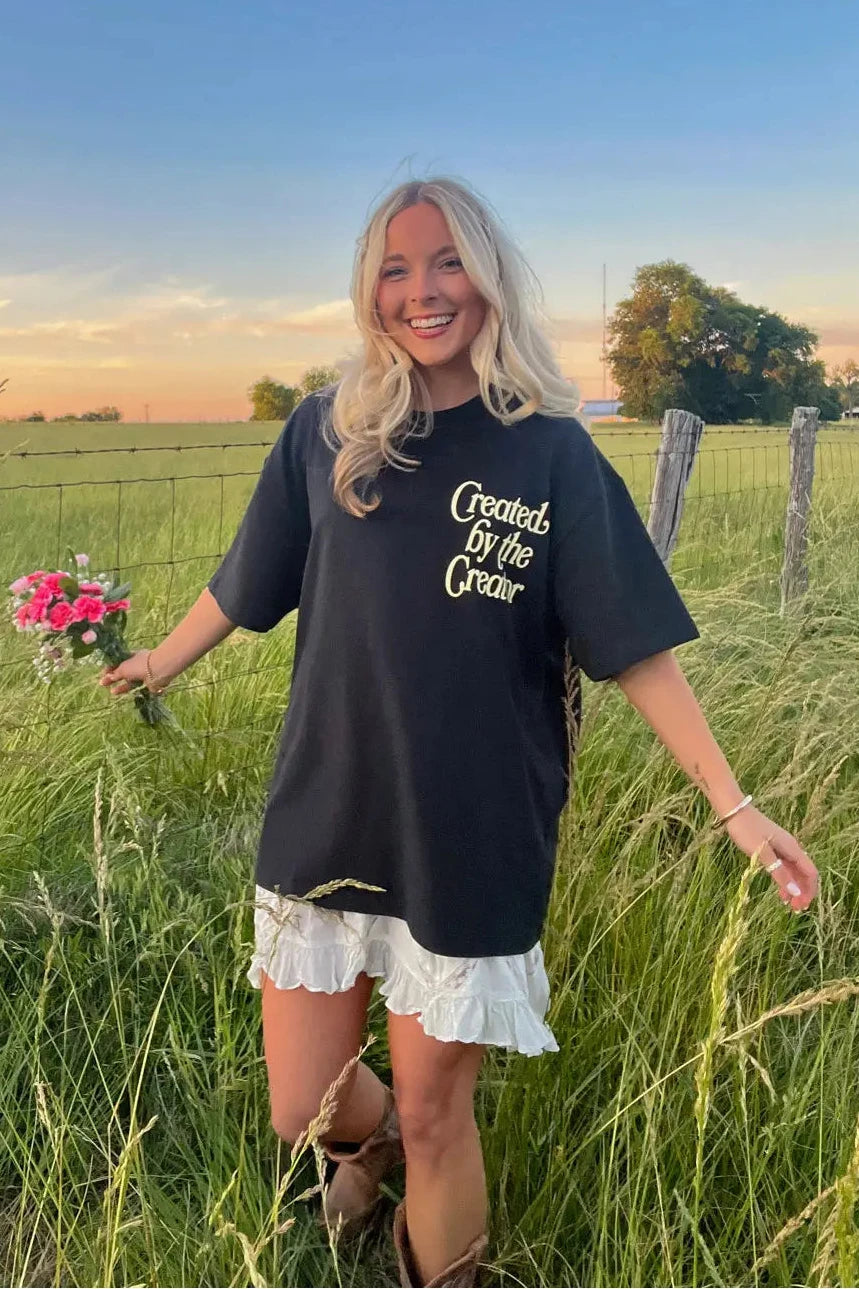 Woman in a black t-shirt with text standing in a field holding flowers.