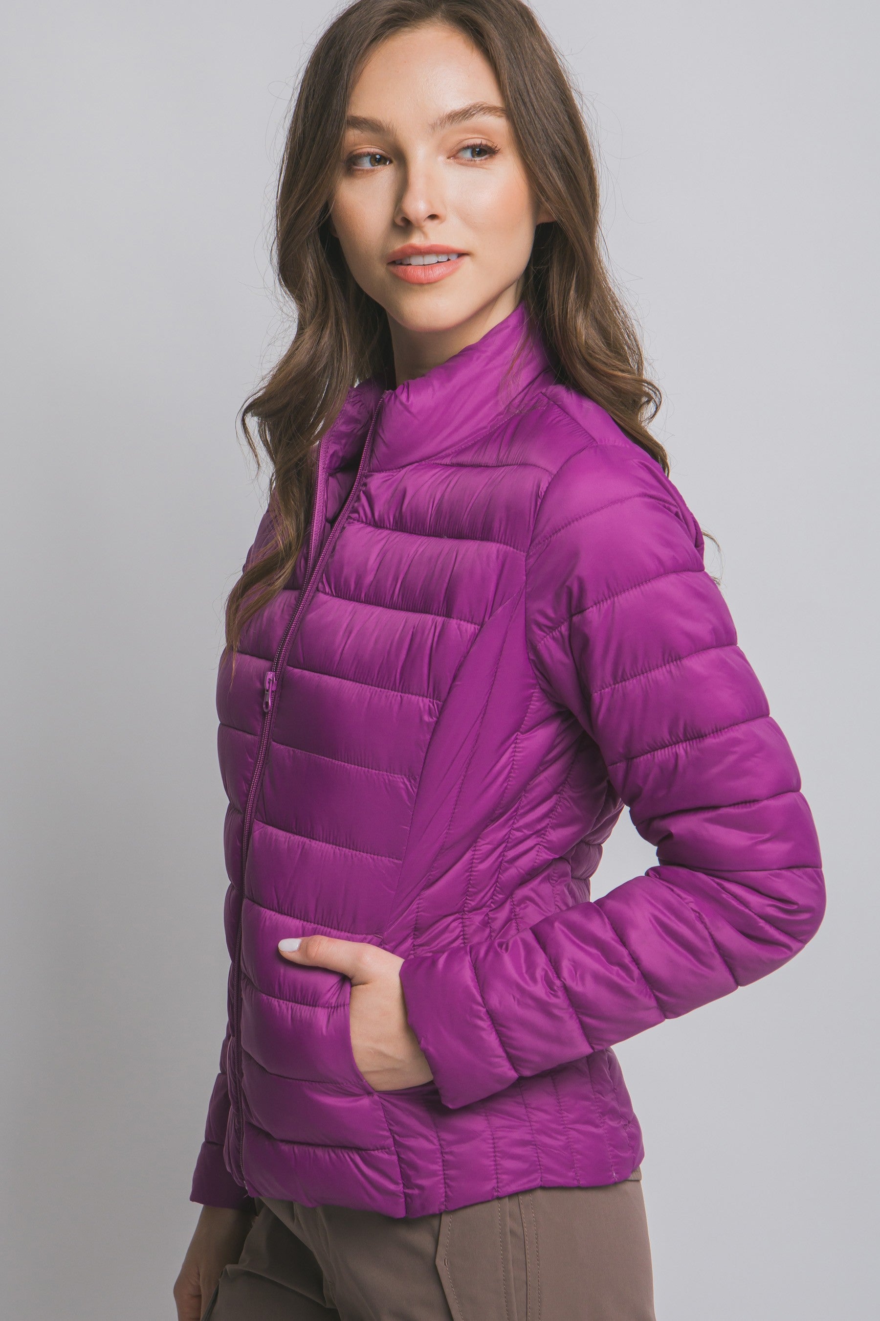 Woman wearing a purple puffer jacket against a plain background