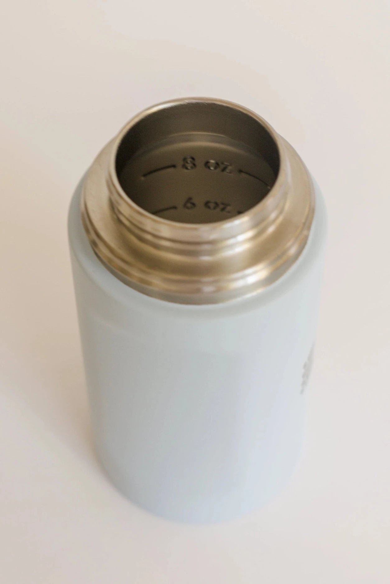 Light blue thermos with silver lid on a beige background