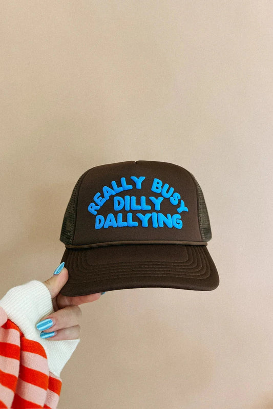 Black trucker hat with blue text held by a person against a beige background