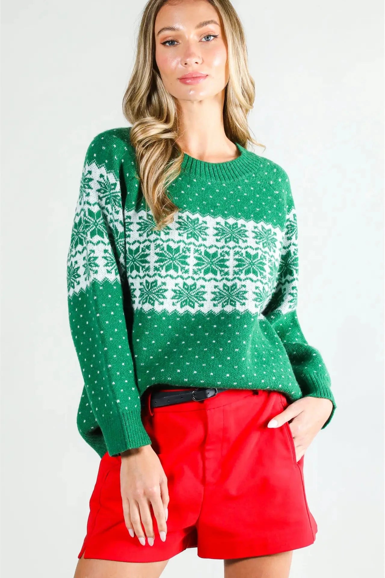 Woman wearing a green sweater with white patterns and red shorts on a white background