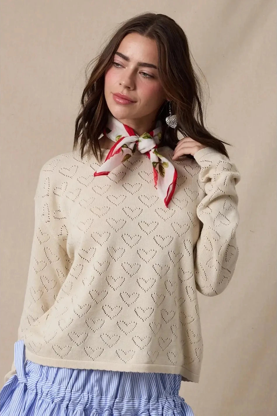 Woman wearing a cream sweater with a pattern and a red scarf, standing against a beige background