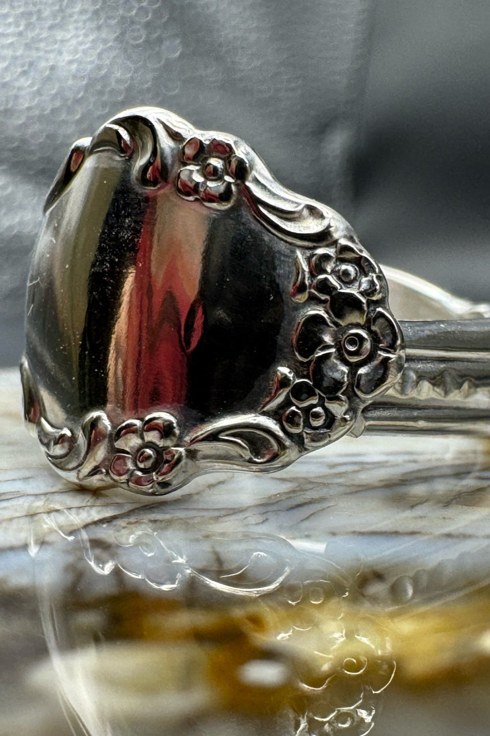 Silver ring with intricate design on a reflective surface