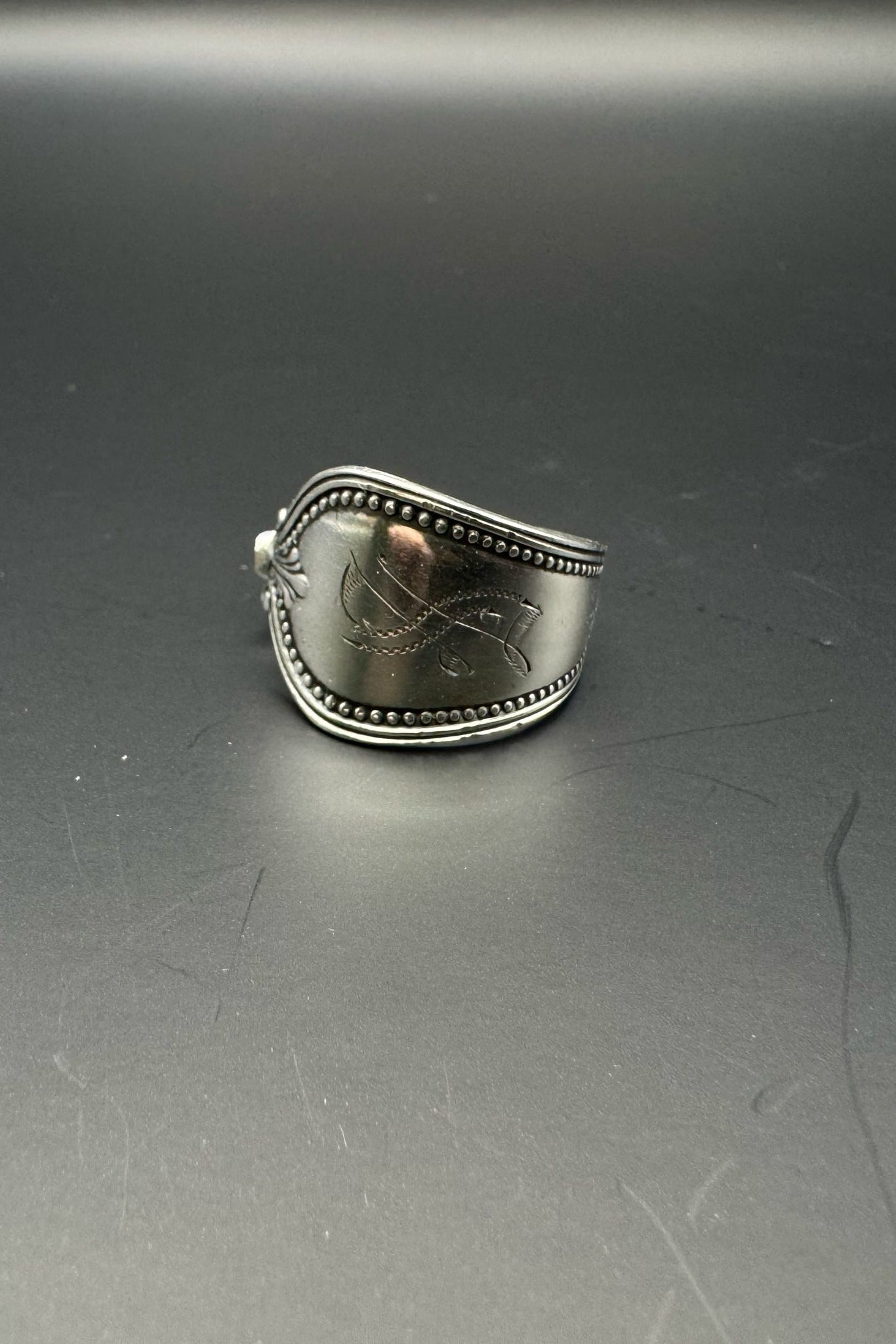 Silver ring with engraved design on a gray surface