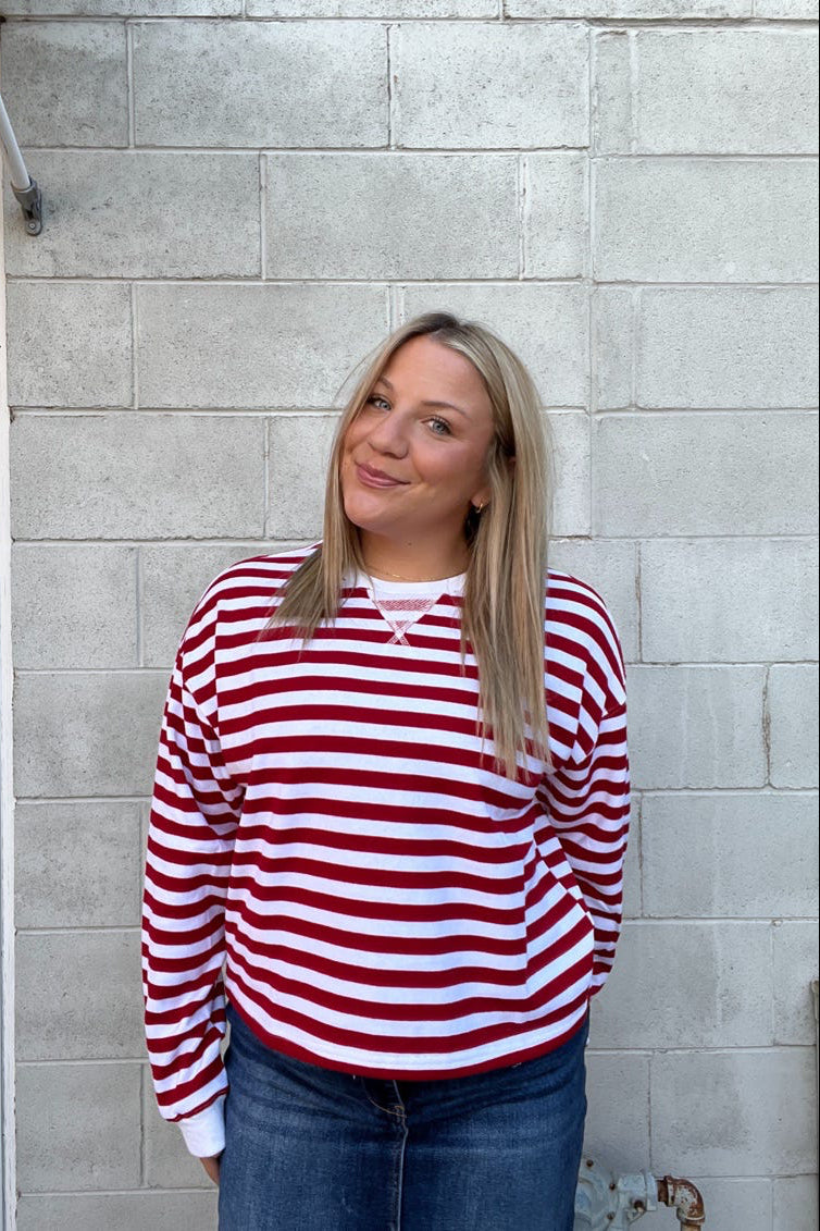 Person wearing a red and white striped shirt standing against a gray brick wall.
