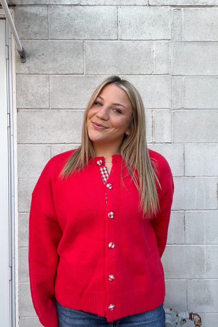 Person wearing a red cardigan standing against a gray brick wall.