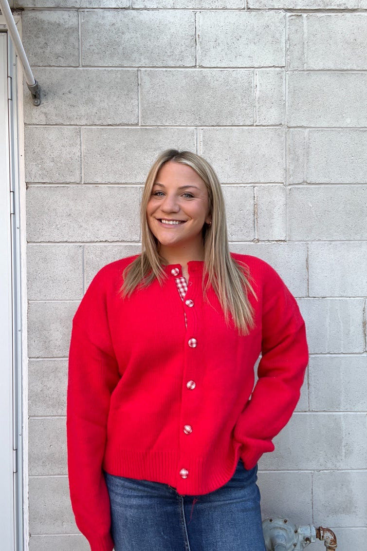 Person wearing a red cardigan standing against a gray brick wall.