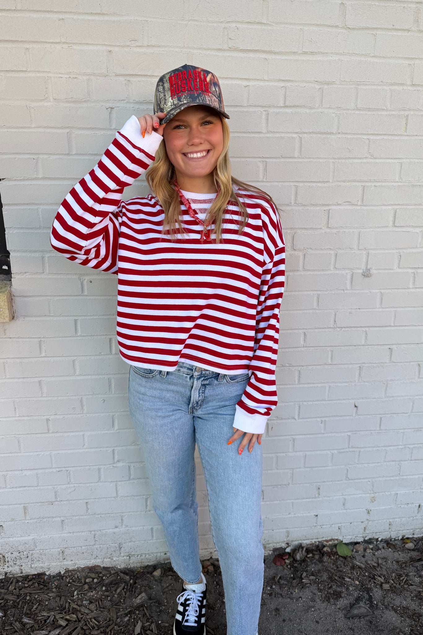 Person wearing a red and white striped shirt and blue jeans, standing against a white brick wall.