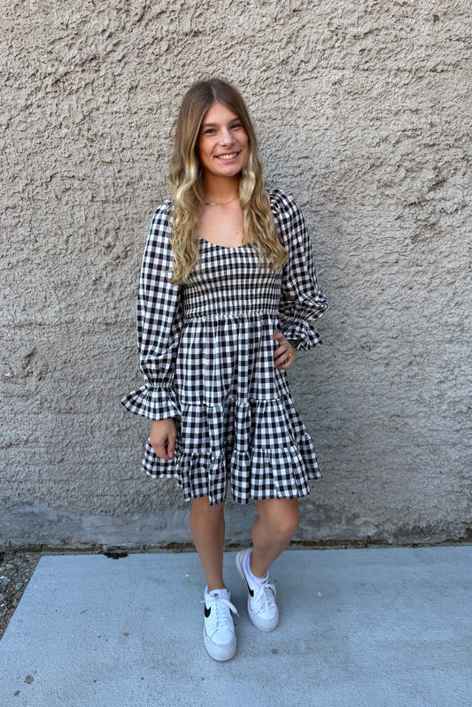 Young girl wearing a black and white checkered dress against a textured wall.