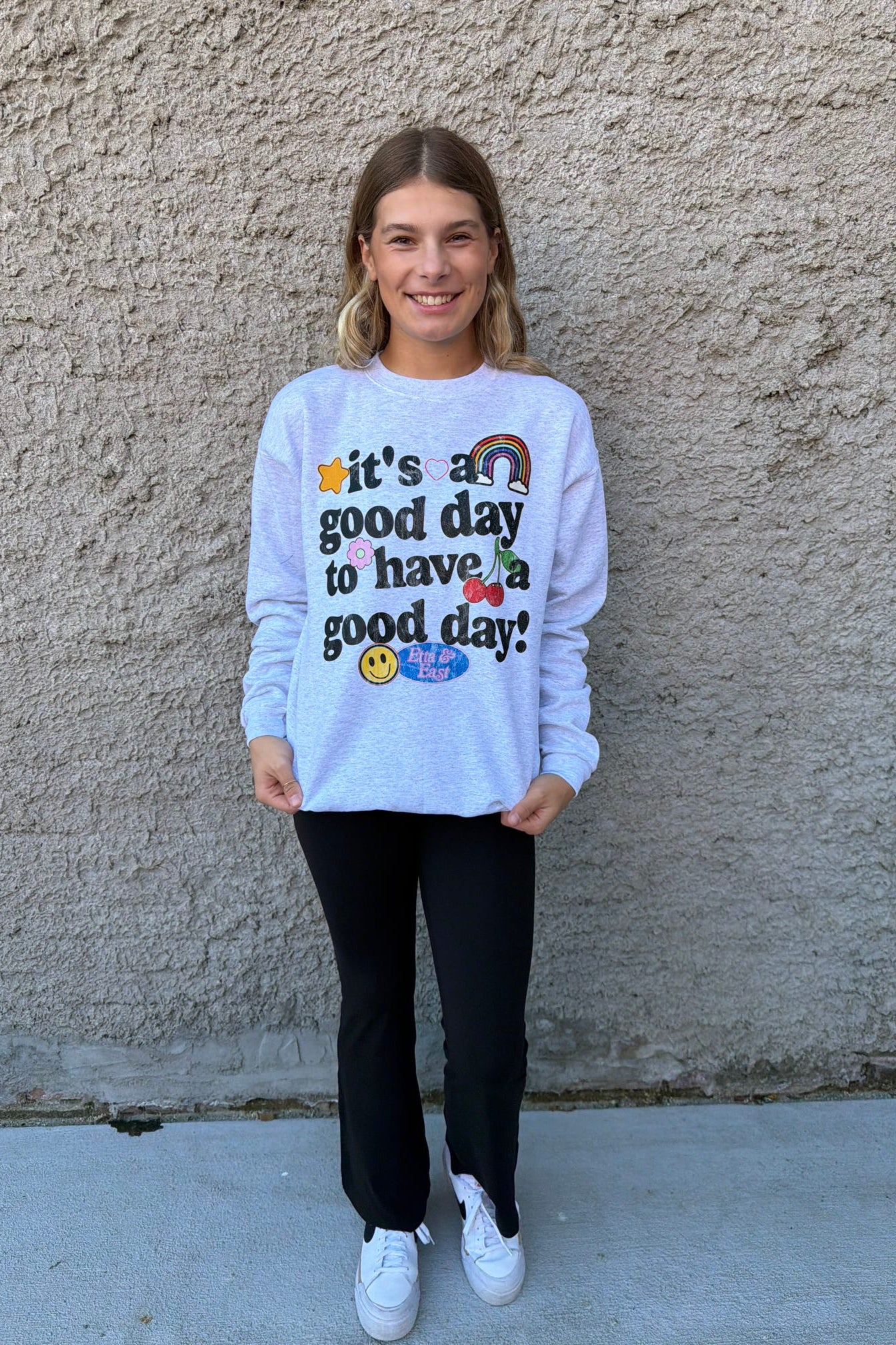 Person wearing a white sweatshirt with a motivational quote against a beige wall.