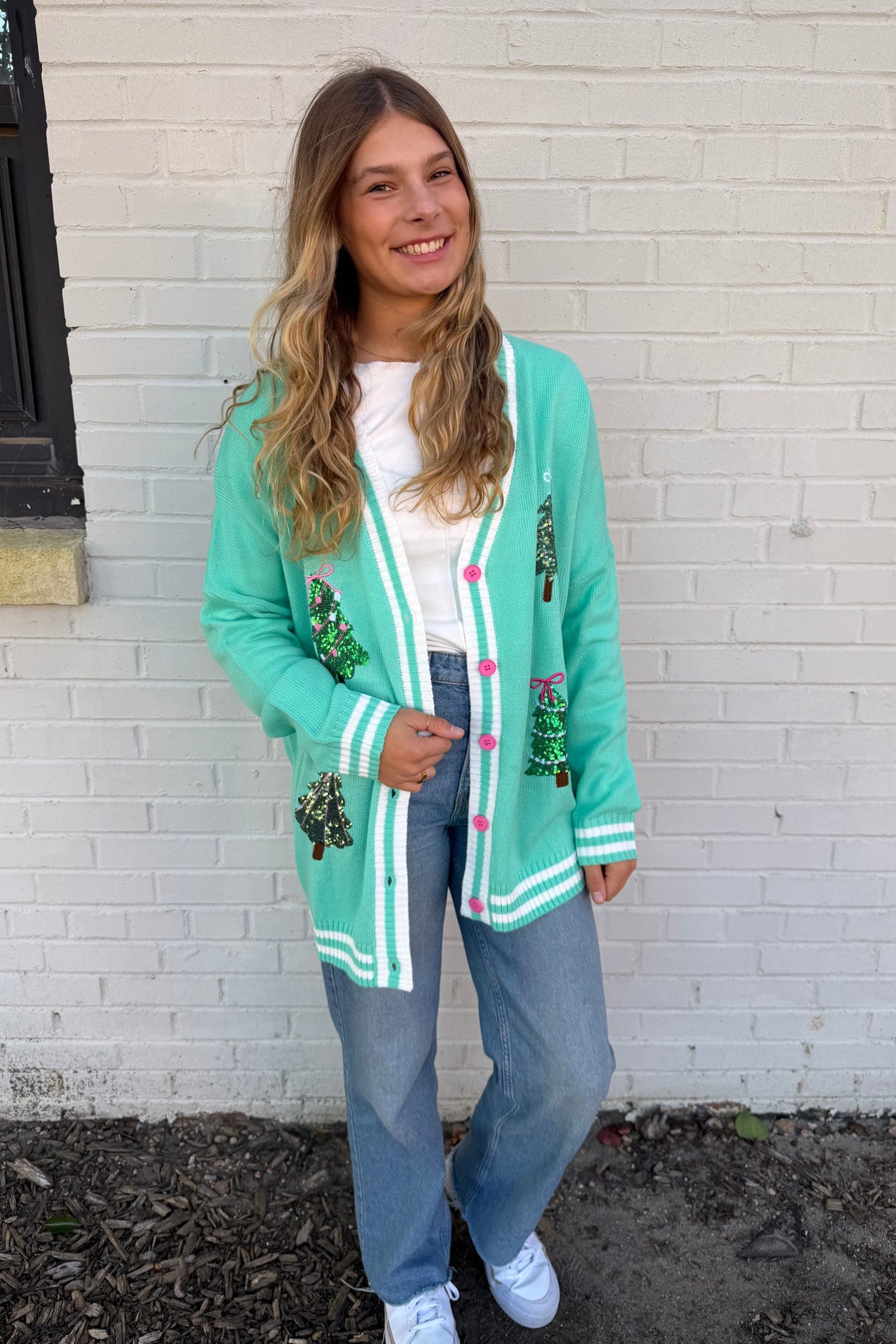 Person wearing a green cardigan with decorative buttons against a white brick wall.
