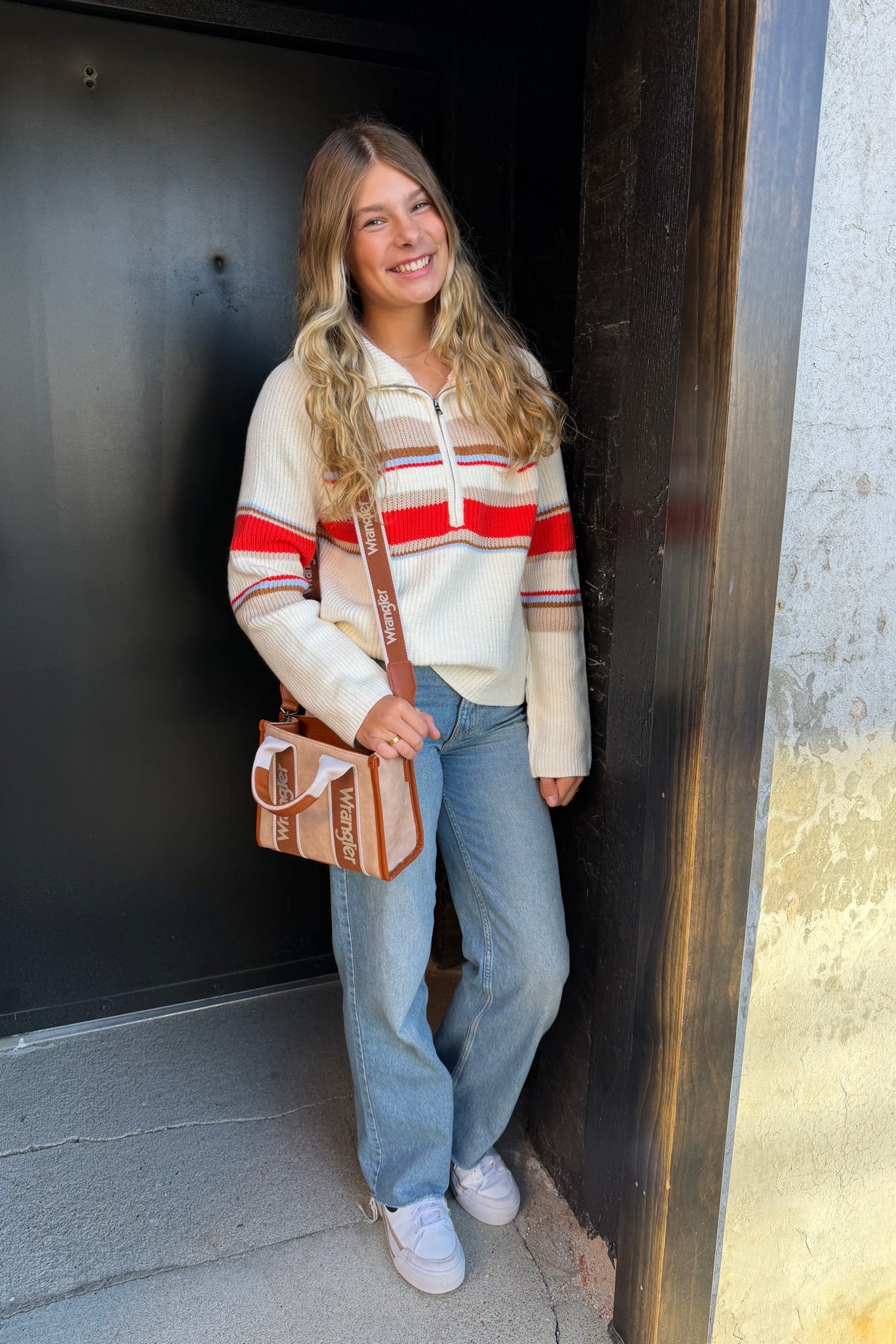 Woman wearing a striped sweater and jeans, standing in a doorway.