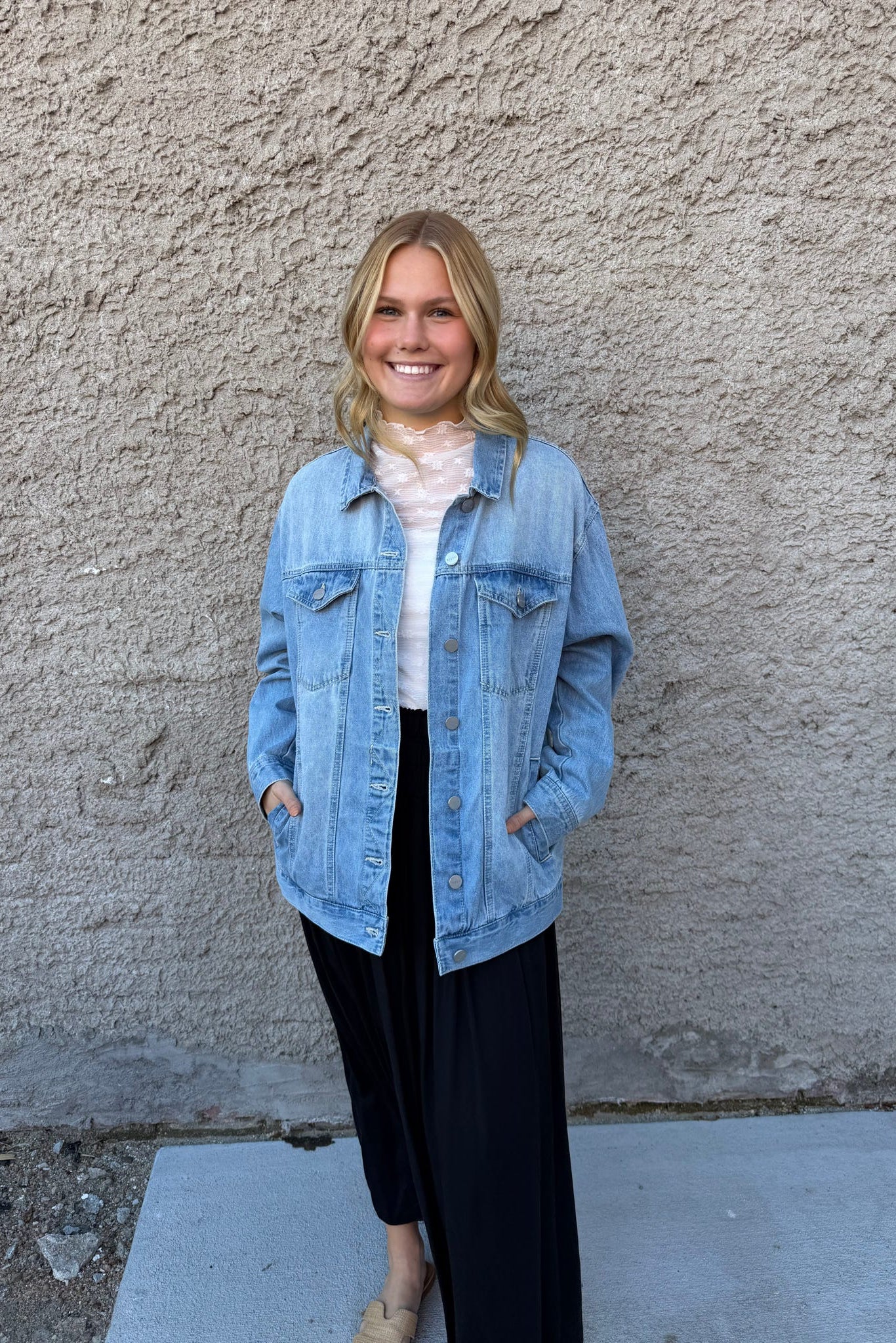 Woman wearing a denim jacket standing against a plain wall.
