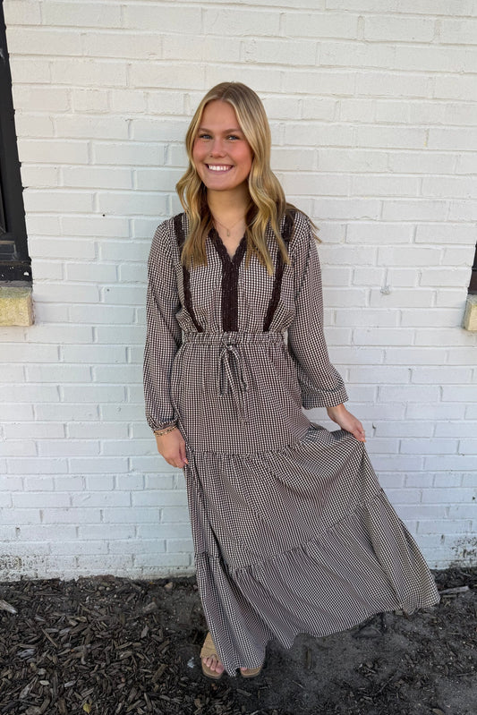 Woman wearing a long, patterned dress standing against a white brick wall.