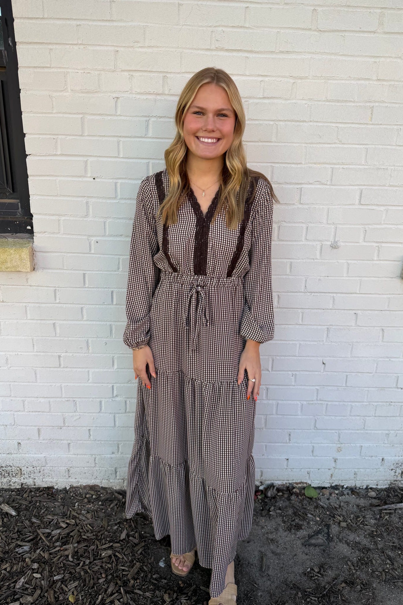 Woman wearing a long, patterned dress standing against a white brick wall.