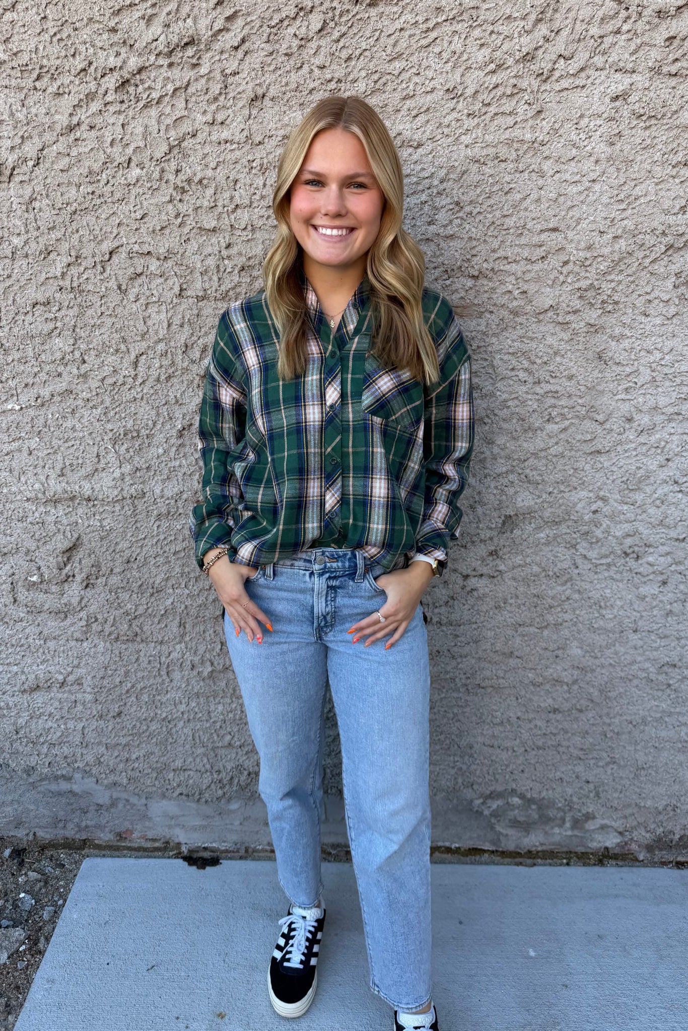 Person wearing a plaid shirt and jeans standing against a textured wall.