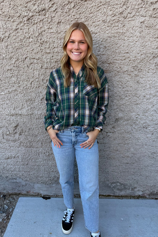 Person wearing a plaid shirt and jeans standing against a textured wall.