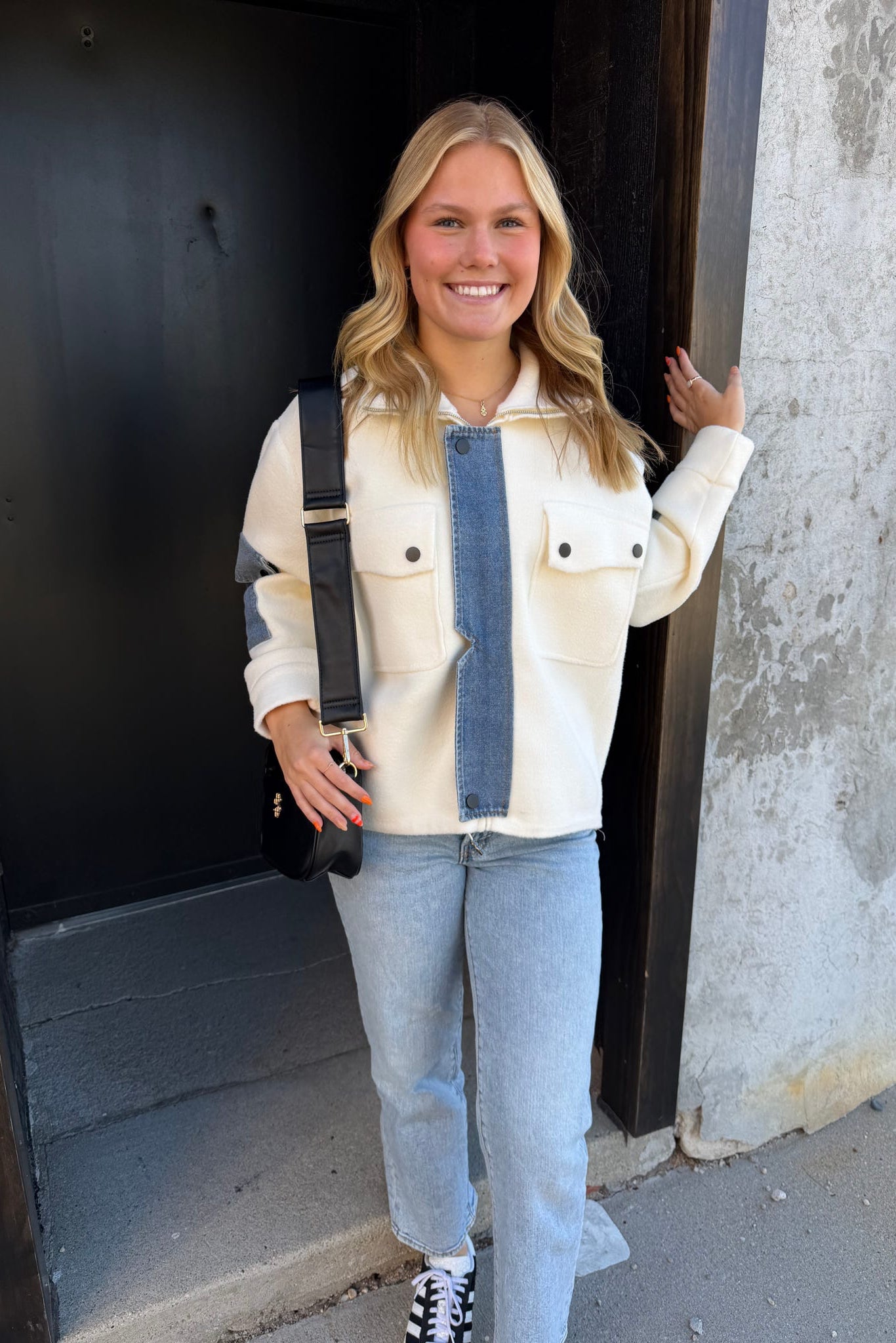 Woman standing outside a building wearing a white jacket and light blue jeans.