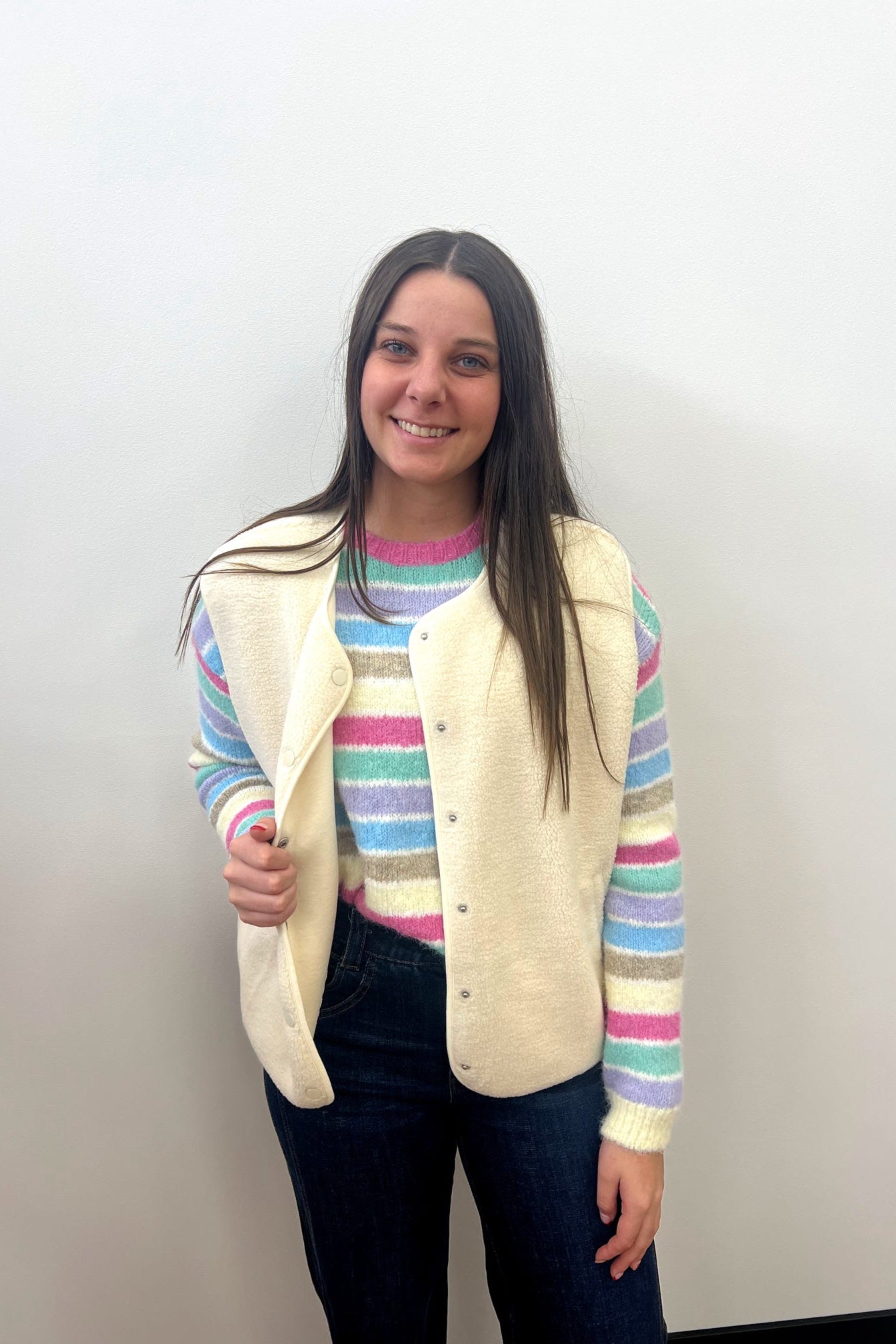 Woman wearing a striped sweater and cream vest against a plain background