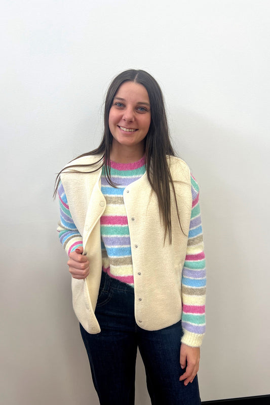 Woman wearing a striped sweater and cream vest against a plain background