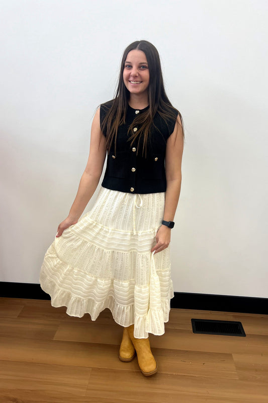 Woman wearing a black sleeveless top and white ruffled skirt with yellow shoes on a plain background