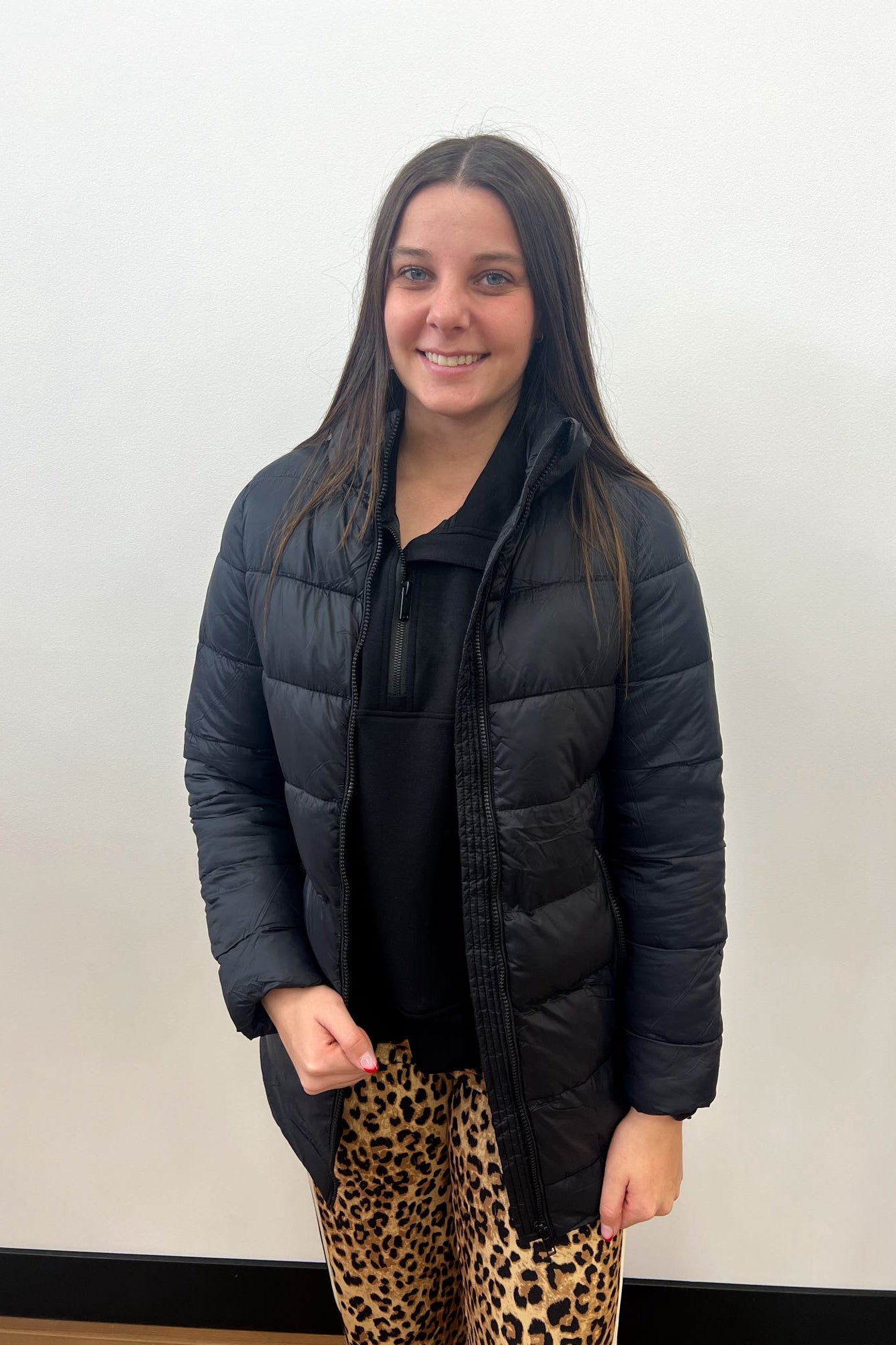 Person wearing a black puffer jacket and leopard print pants against a plain background