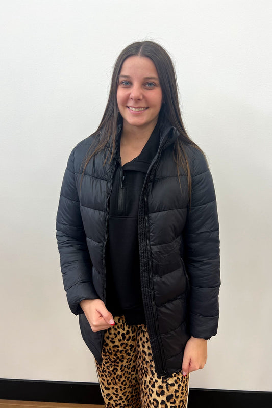 Person wearing a black puffer jacket and leopard print pants against a plain background